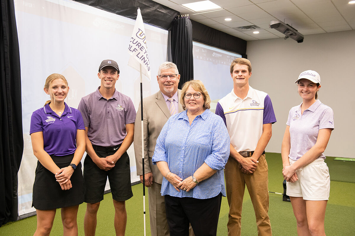 Men and women golf players standing with the former president and his wife in the golf simulator