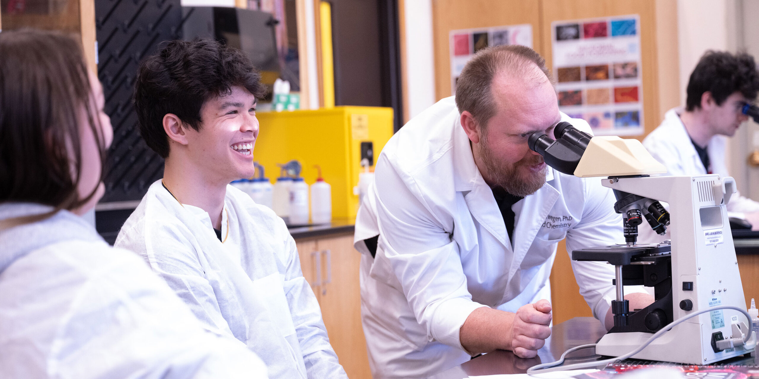 Biology professor helping students with a microscope.