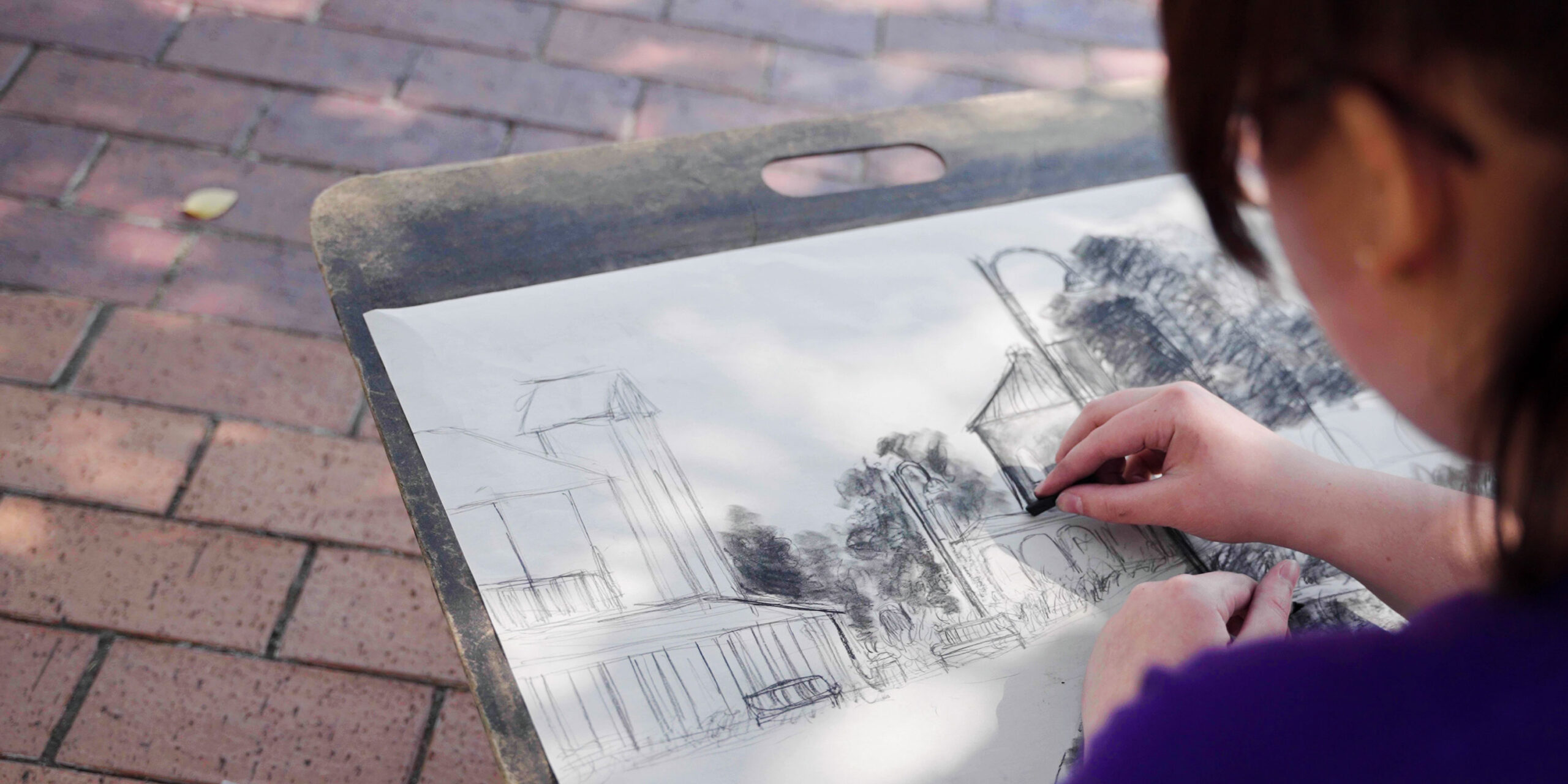 Student drawing a landscape of Northwestern while sitting outside.