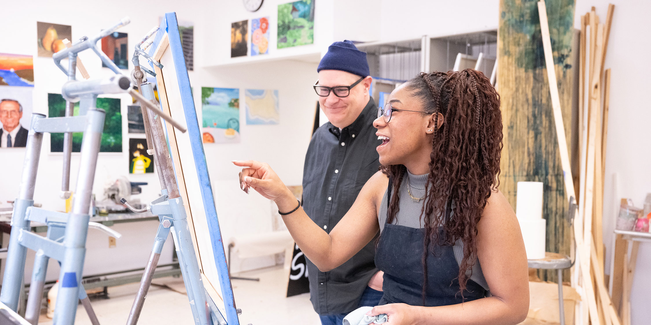 Diverse female student working on a painting and chatting about it with her art professor.
