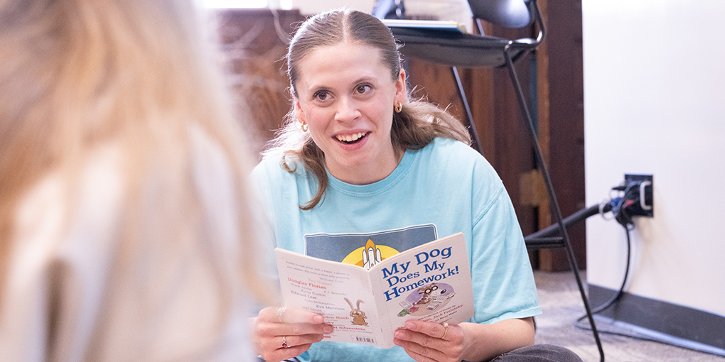Female student reading a book to a classmate.