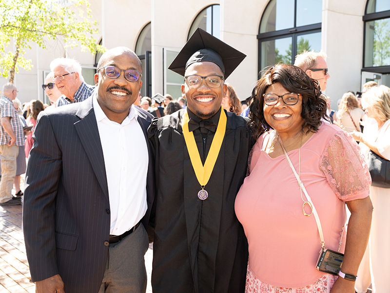 Graduate in cap and gown with his parents.