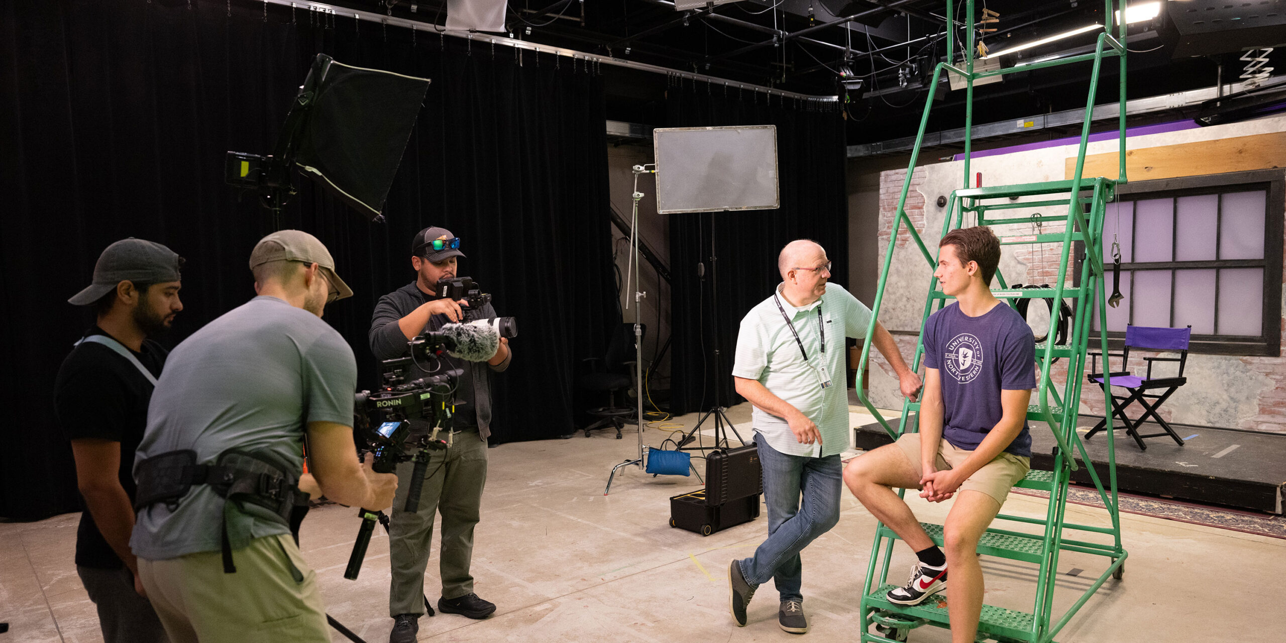 Student and professor talking while being filmed by a camera crew in the studio.