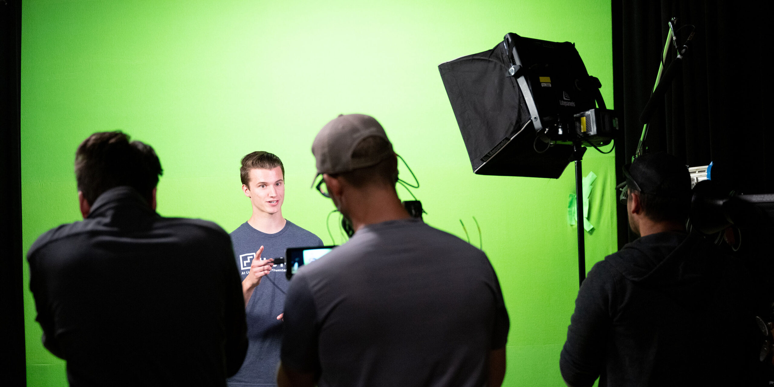 Male student being filmed in front of a green screen.