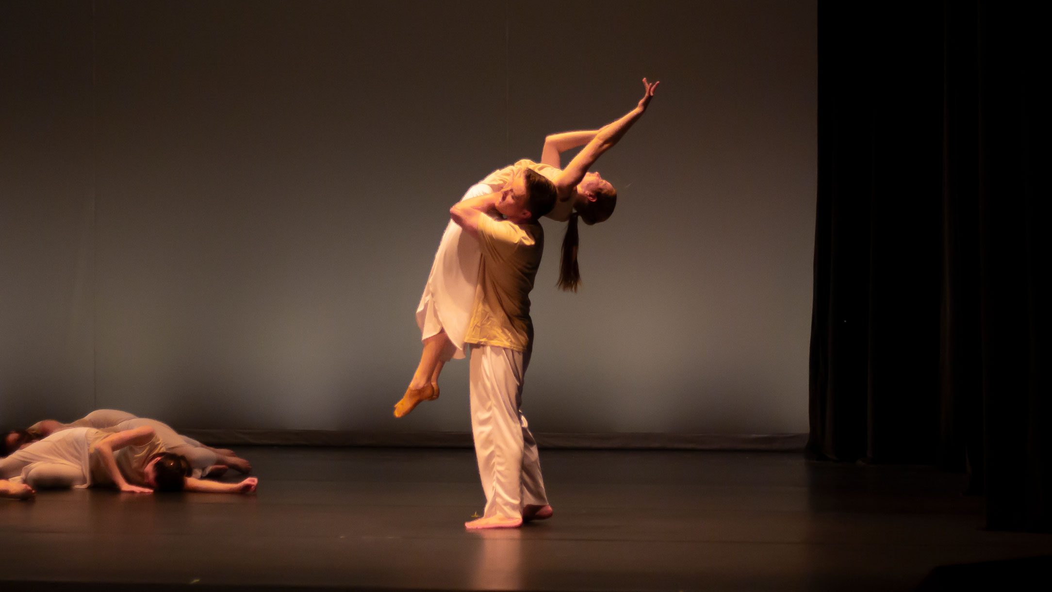 Dance student lifting another student on stage mid-performance.