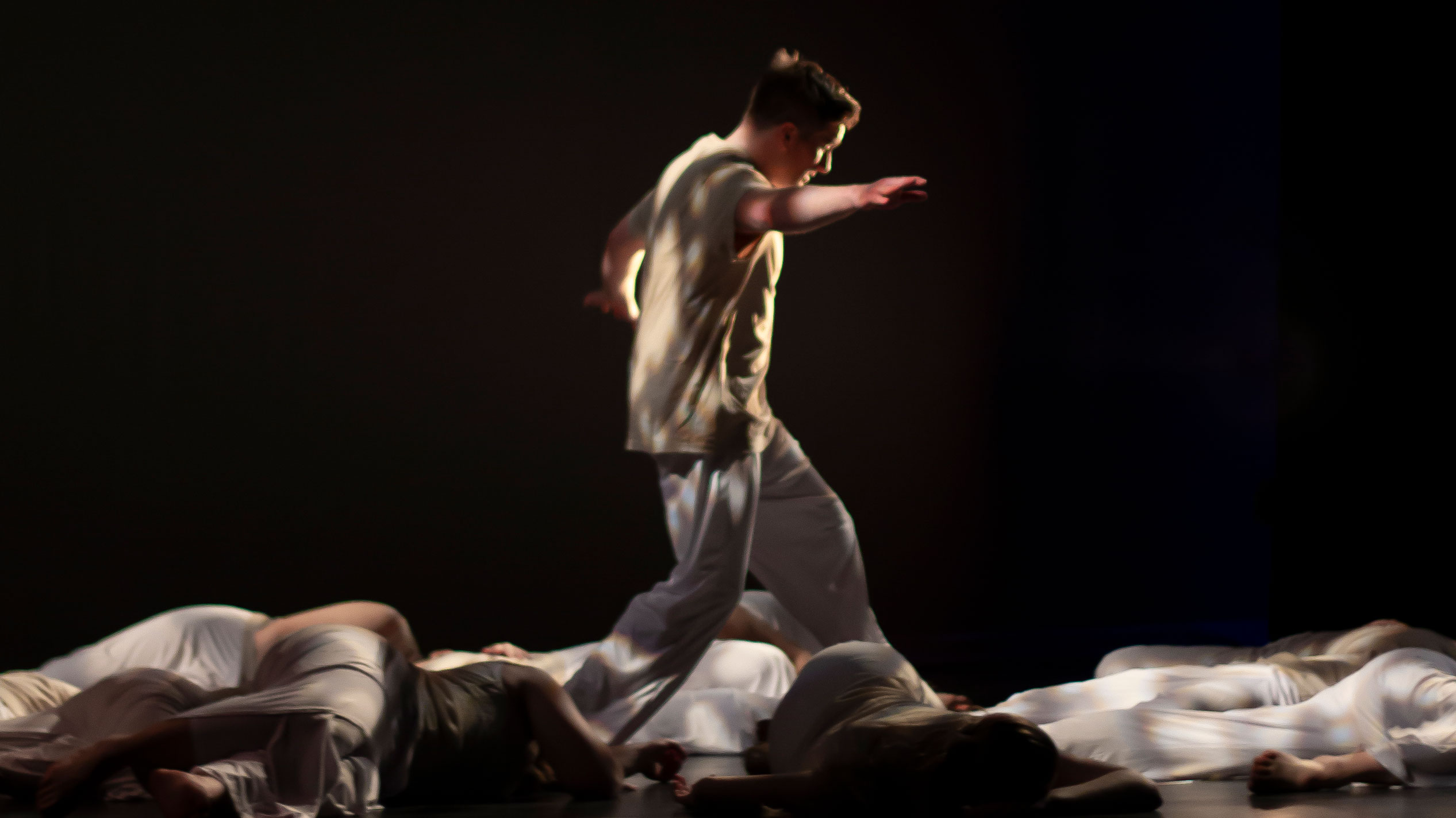 Dance student mid performance dancing on stage surrounded by other students laying on the stage.